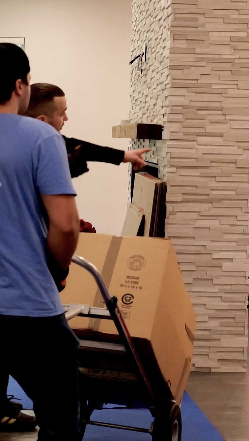 Keep Moving movers in blue shirts load a box on a hand truck next to a stone fireplace during a Toronto move
